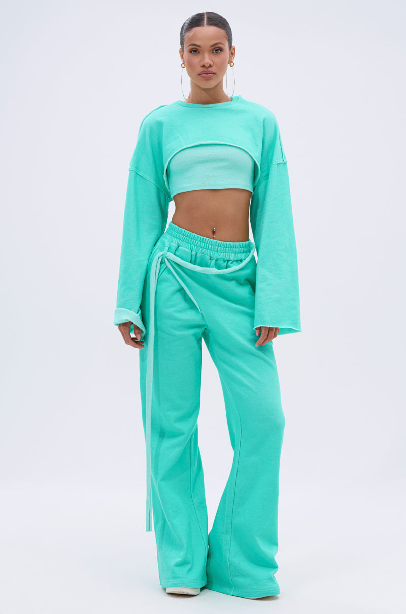 A person stands facing forward, wearing the ISSA JOGGER PANT IN TIFFANY—wide-leg joggers with a high-rise elastic waistband and a matching long-sleeve crop top—set against a plain, light-colored background. 7