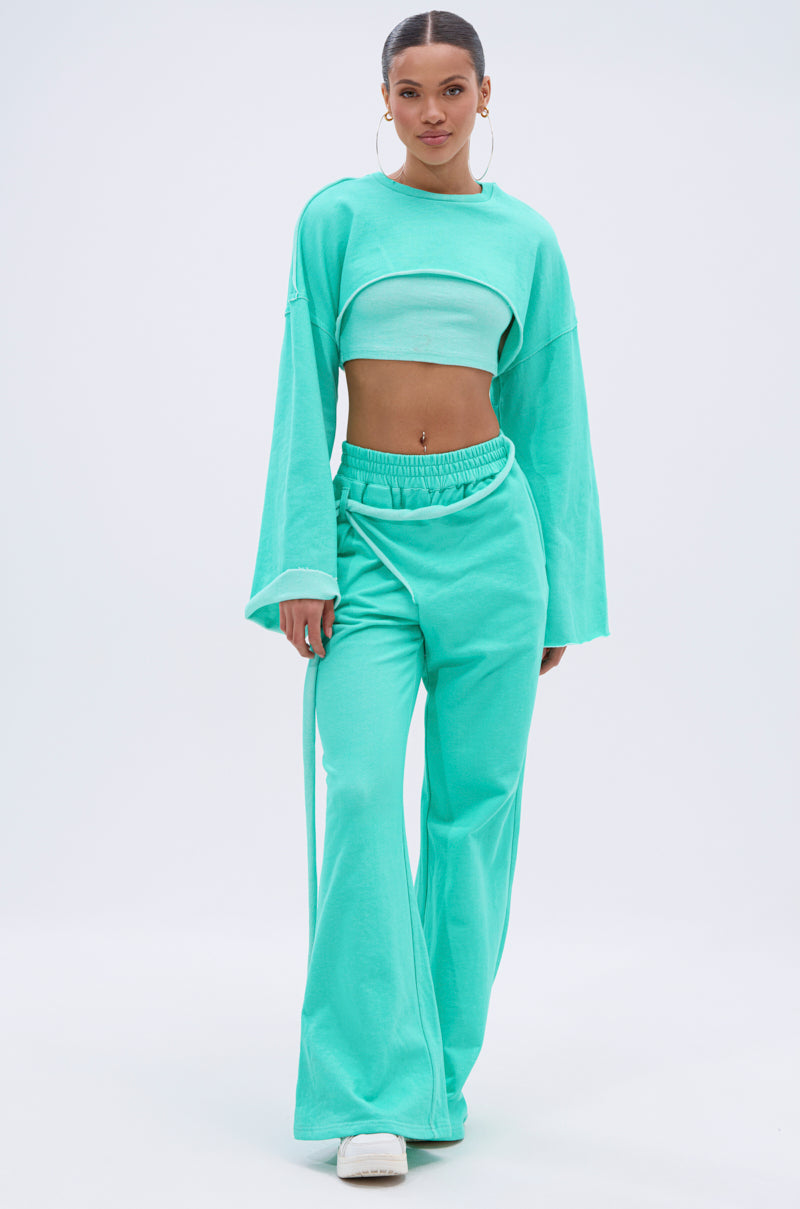 A woman wears a turquoise cropped long-sleeve top and the ISSA JOGGER PANT IN TIFFANY, featuring a high-rise elastic waistband, paired with white sneakers against a plain light background. 8