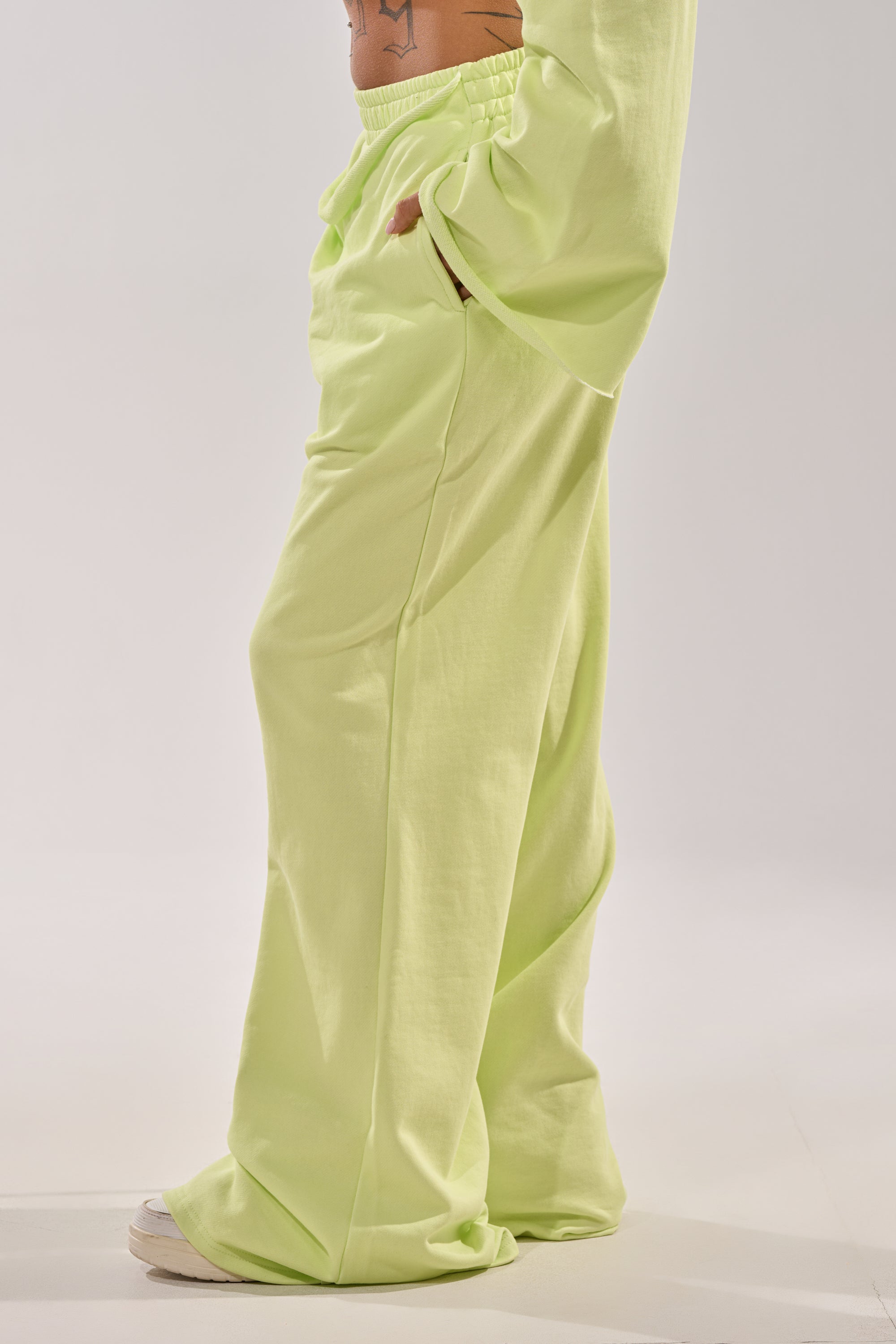 The lower half of a person is shown against a plain light background, wearing the TRY ME BABY WIDE LEG JOGGER—loose-fitting, lime sweatpants with a high-rise elastic waistband and pockets—paired with a matching long-sleeve top. 4