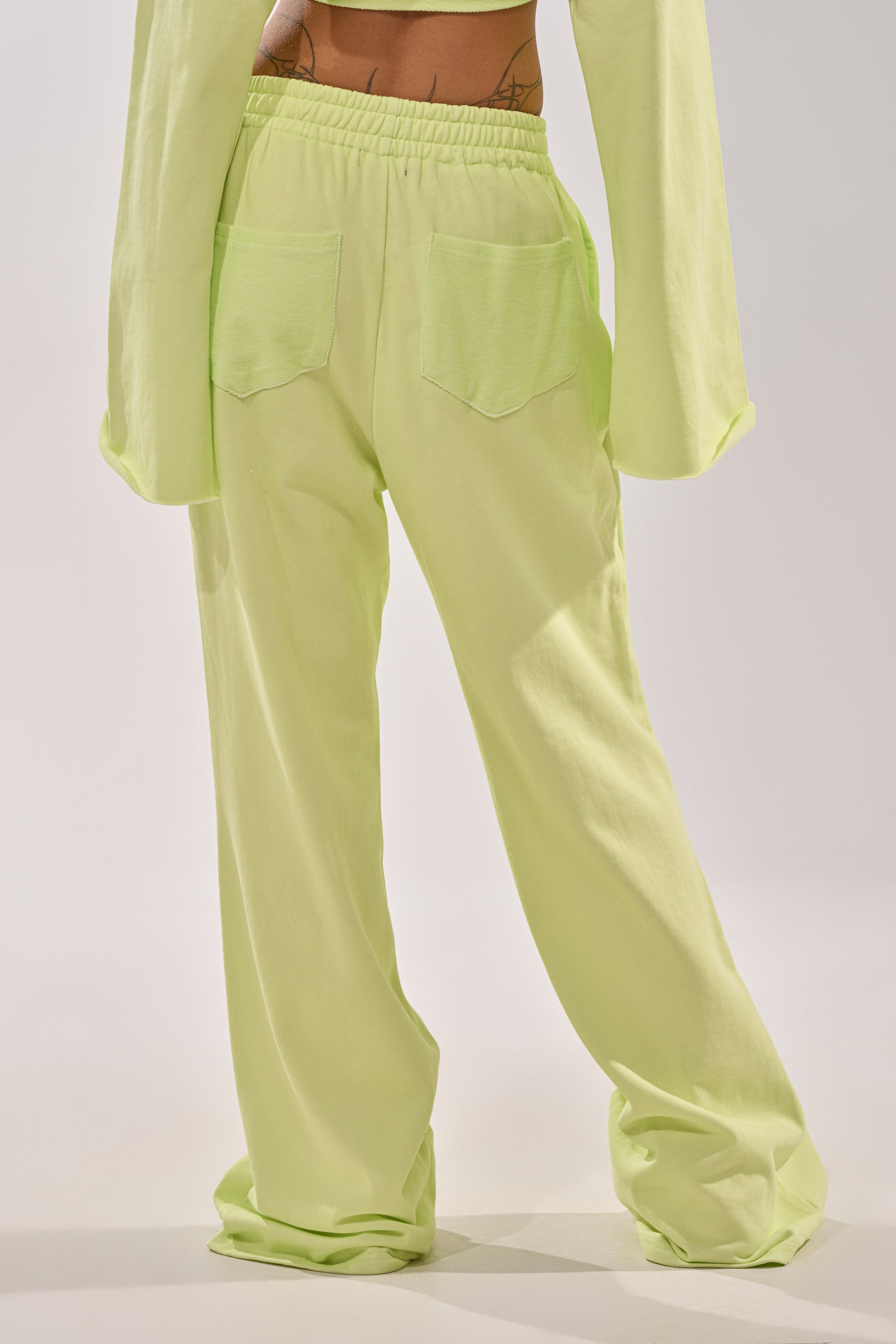 Someone wearing the TRY ME BABY WIDE LEG JOGGER in lime, featuring a high-rise elastic waistband, two back pockets, and a matching long-sleeve top, viewed from behind—combining streetwear style with comfort. 5