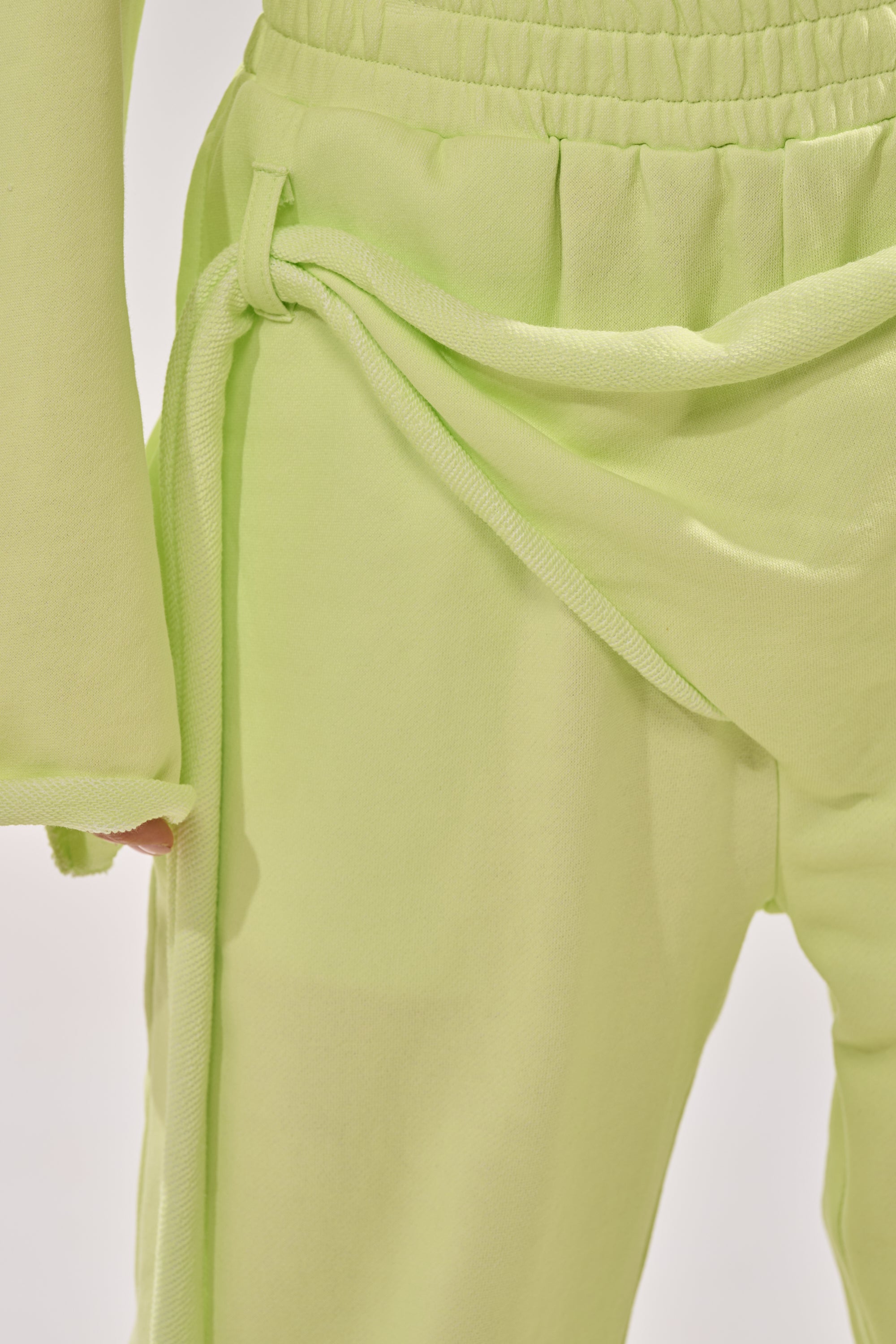 Close-up of a person wearing the TRY ME BABY WIDE LEG JOGGER in light green, featuring a high-rise fit with an elastic waistband and side-tied belt. A matching light green top’s sleeve is partially visible. 7