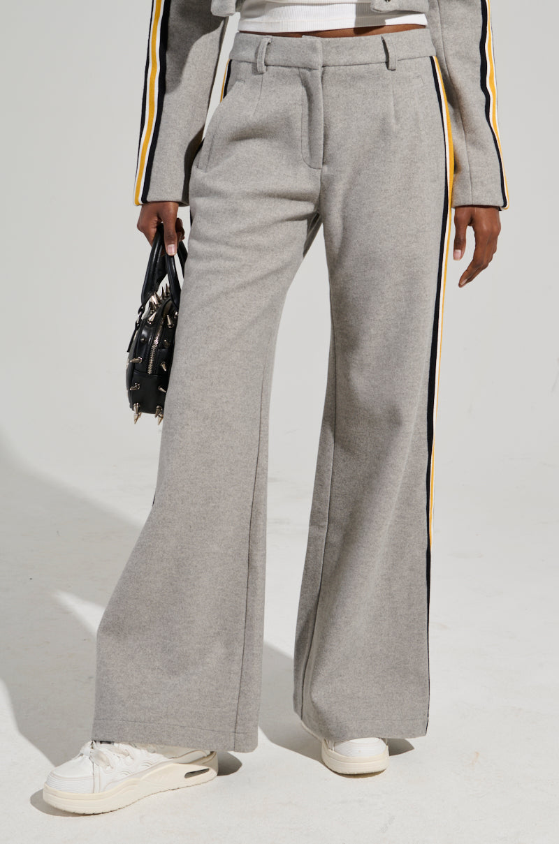 A person wearing the STAY WITH ME WIDE LEG PANT in high-rise gray, featuring color block stripes in yellow and black, paired with white sneakers. The person is holding a small black handbag, and a matching gray top with similar stripes is partially visible.