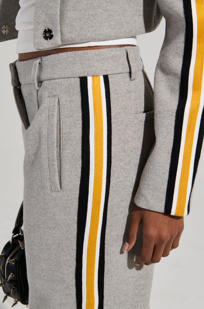 A person wears the STAY WITH ME WIDE LEG PANT in gray, which showcases color block stripes. The outfit is paired with a matching jacket and a white top worn underneath. The individual accessorizes with a small black handbag adorned with silver studs, which pairs perfectly with the high-rise design.