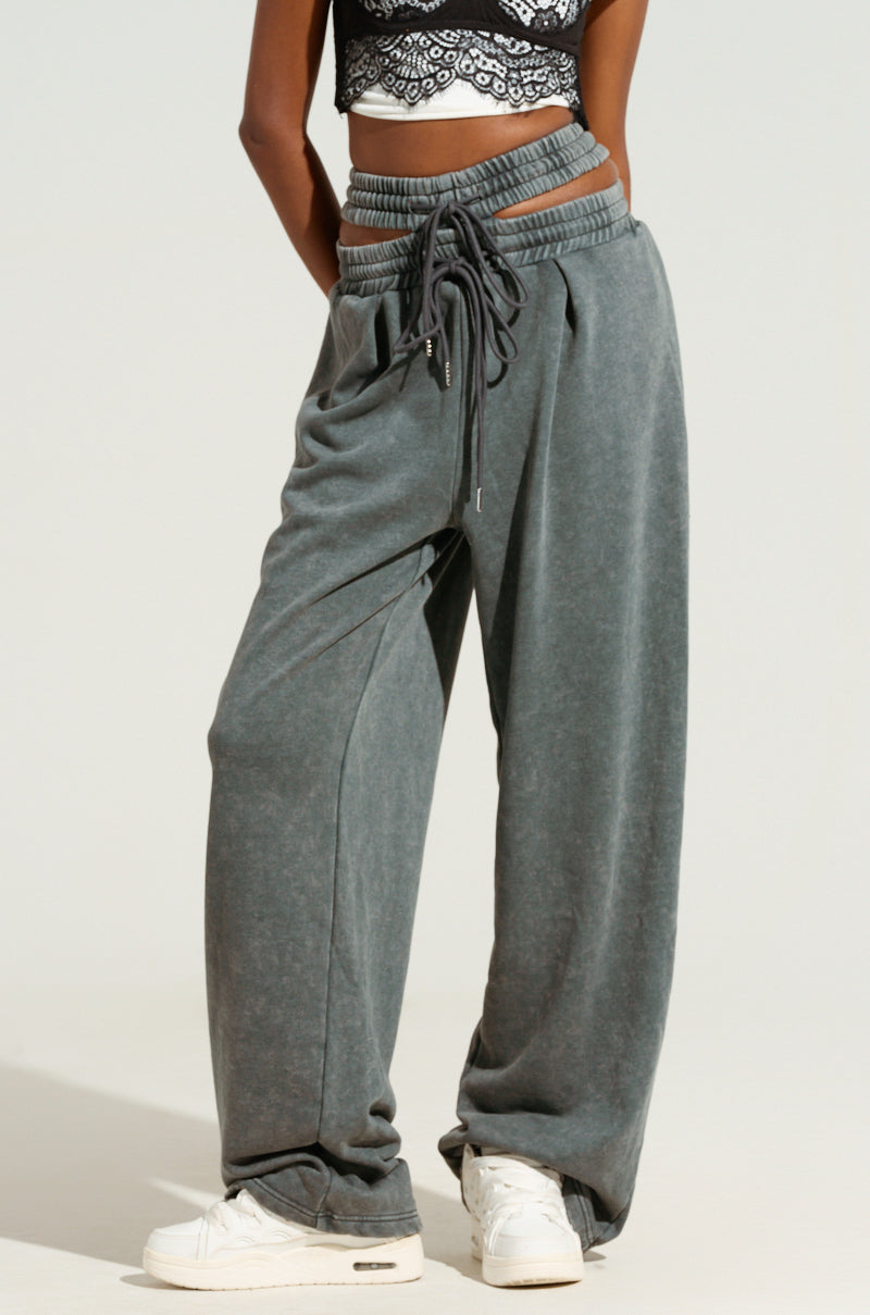 Against a plain background, a person stands wearing the NEXT UP IS ME SWEATPANT, featuring a dual shirred elastic waistband and wide leg silhouette, paired with a lace-patterned crop top. The look is completed with white sneakers for an added touch of casual elegance.