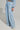A person dressed in HONEY HONEY WIDE LEG PANTS, a light blue, cotton blend top and matching wide-leg pants featuring a high-rise fit with a drawstring waist, forming a loose-fitting ensemble with pockets. They complete the look with white sneakers against a plain gray backdrop.