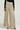 A person is wearing a black sweater paired with the stunning FEELING GODLY PLEATED HIGH WAIST PANT IN GOLD, made from a dazzling gold metallic knit weave. They complete the look with gold high-heeled sandals against a plain, light-colored background.