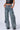 A person is wearing the EVERY LITTLE THING SHE DOES DENIM PANT, featuring a high-waisted, wide-leg silhouette with cargo pockets and multiple straps, paired with a sleek black sleeveless leather top. With their hands casually in the front pockets of the jeans and standing against a plain background, the outfit exudes a trendy, edgy style.