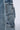 Close-up of the EVERY LITTLE THING SHE DOES DENIM PANT, showcasing blue denim cargo pocket jeans with multiple pockets and a detachable strap on the side. The fabric exhibits a slightly faded, distressed look with metal hardware accents, including clips for the strap. Featuring a wide leg silhouette, the background remains plain and minimally visible.