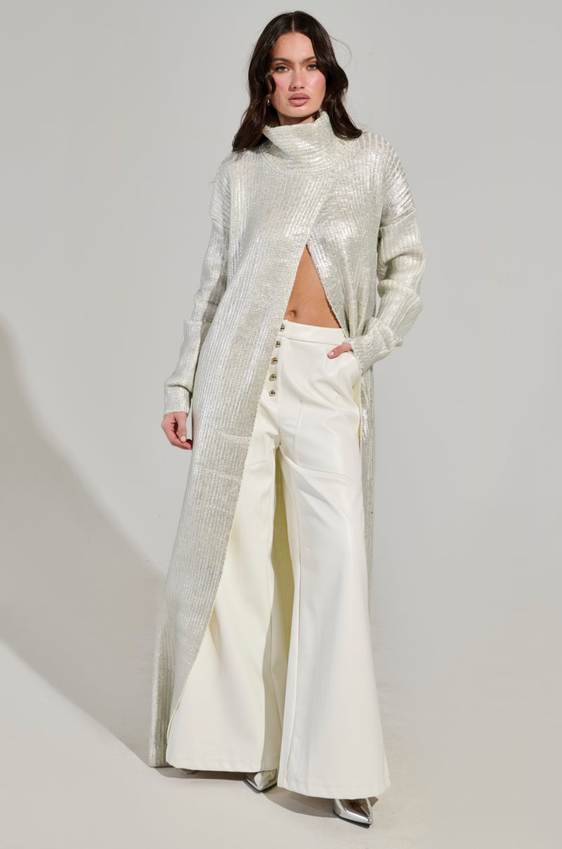 A person stands confidently wearing a long, shimmering silver coat over the ASHLYN FAUX LEATHER PANT IN WHITE, which features a mid-rise and wide-leg silhouette. The coat is slightly open at the front, revealing a glimpse of the midriff against a plain and light-colored background. 1