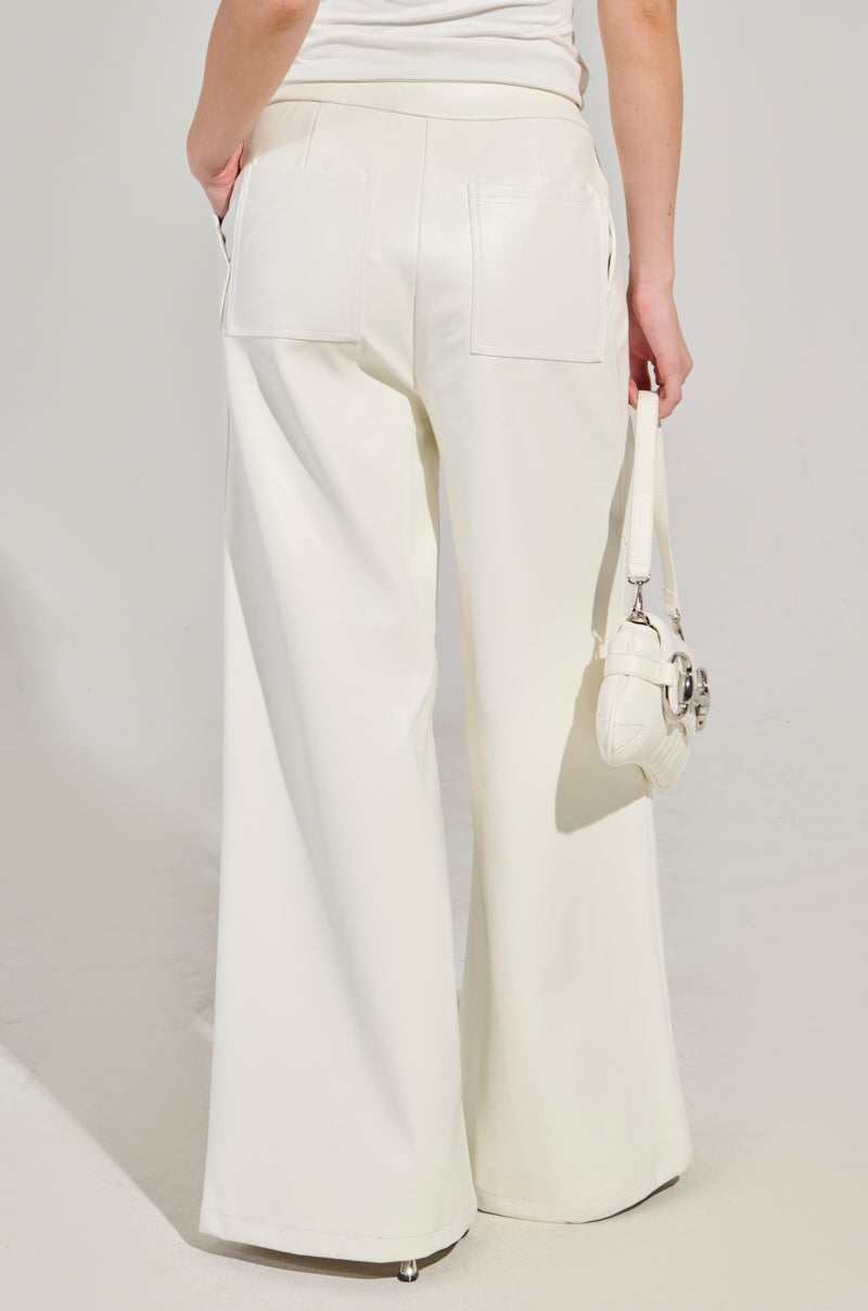 A person is captured from behind, showcasing the elegant flow of ASHLYN Faux Leather Pants in white, paired with a small white handbag. The neutral setting with soft lighting highlights the stylish design of these high-waisted, wide-leg silhouette pants. 4