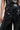 A close-up of someone wearing the ASHLYN FAUX LEATHER PANT IN BLACK highlights its shiny faux leather fabric, high-rise design with five buttons, and wide-leg silhouette. The stylish cutout designs at the top offer a unique and edgy fashion statement.