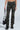 A person wearing MAKE A MOVE CAMO PANT with ruched legs and black chunky boots holds a small black bag against a plain, light-colored background.