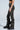 Standing in profile, a person clad in a black crop top and MAKE A MOVE CAMO PANT with cargo-style pockets showcases a ruched design that complements their black combat boots. A tattoo on their forearm contrasts against the plain, light-colored background.