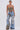 A woman poses confidently against a plain backdrop in the THOUGHT I KNEW YOU RELAXED DENIM WITH BROCADE—high-waisted, wide-leg jeans featuring large rips and floral jacquard panels—paired with a strapless floral bustier and hoop earrings.