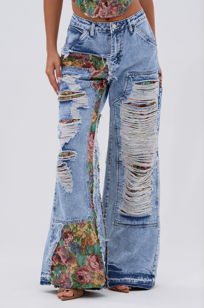 Wearing the THOUGHT I KNEW YOU RELAXED DENIM WITH BROCADE—high-waisted, wide-leg jeans with large rips revealing floral jacquard panels and frayed hems—paired with a floral top for a bold, standout look.