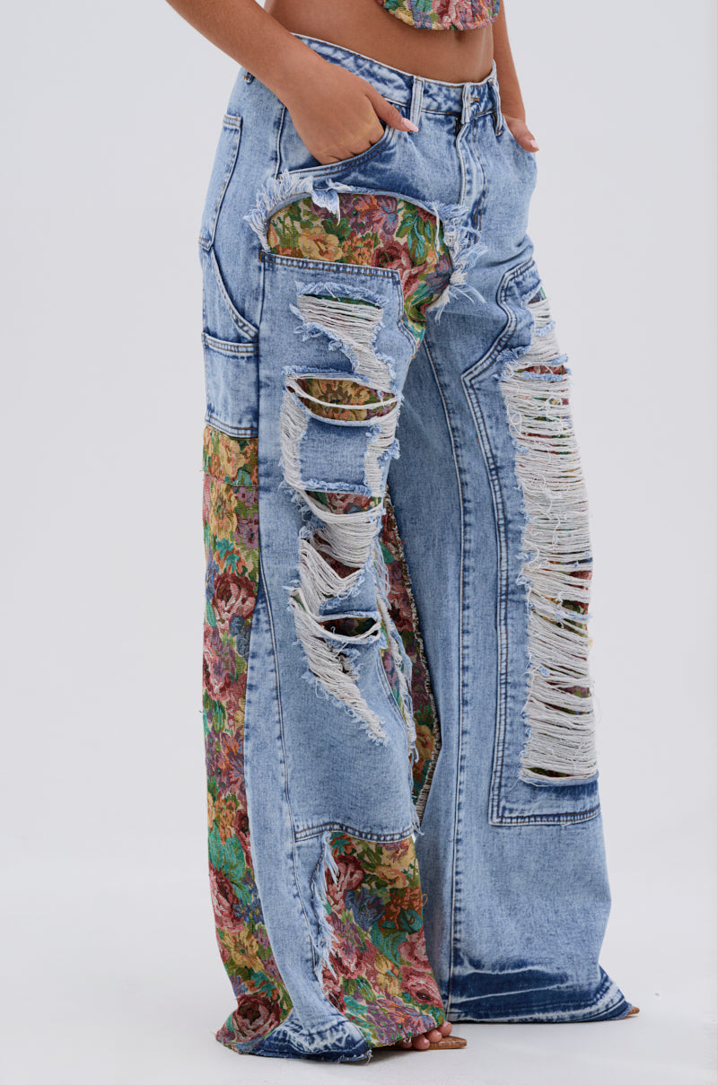 Their hands rest in the pockets of THOUGHT I KNEW YOU RELAXED DENIM WITH BROCADE, high-waisted wide-leg jeans featuring floral brocade fabric patches and distressed, ripped details from the lower torso down.