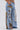 Their hands rest in the pockets of THOUGHT I KNEW YOU RELAXED DENIM WITH BROCADE, high-waisted wide-leg jeans featuring floral brocade fabric patches and distressed, ripped details from the lower torso down.
