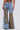 Someone wears the THOUGHT I KNEW YOU RELAXED DENIM WITH BROCADE—high-waisted, wide-leg light blue jeans with large floral brocade patches and multiple pockets—paired with a matching floral crop top. The photo is taken from behind.