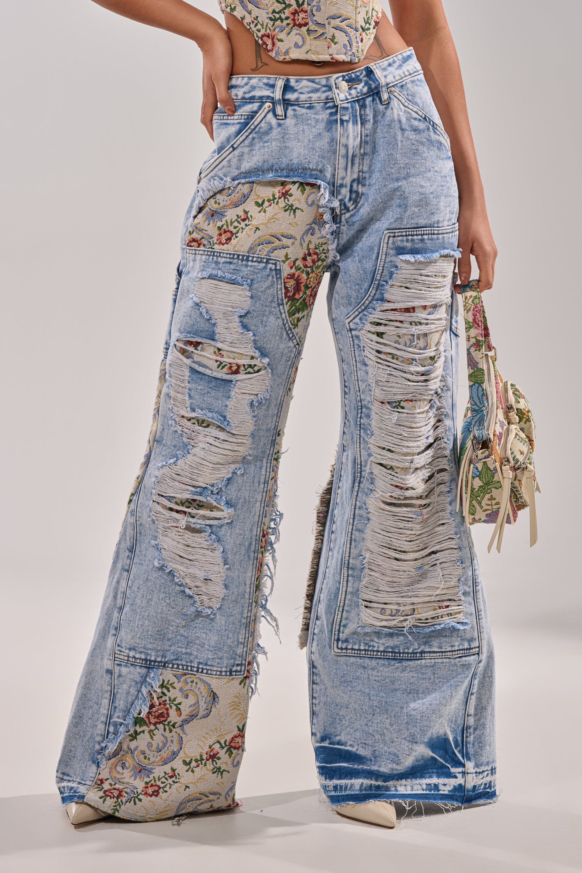 Wearing LANA DISTRESSED JEANS WITH JACQUARD DETAIL—a super-wide silhouette with floral tapestry patches—paired with a coordinating floral top and matching floral handbag. Only the torso and legs are visible. 0