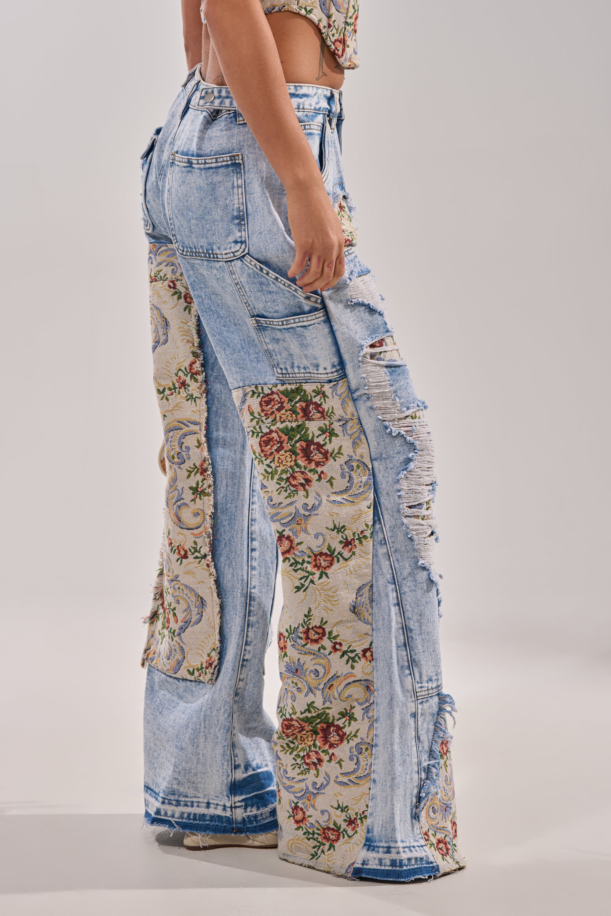 A person wears the LANA DISTRESSED JEANS WITH JACQUARD DETAIL, featuring high-waisted, light-wash denim with tapestry-style jacquard panels, and stands against a plain background. 2