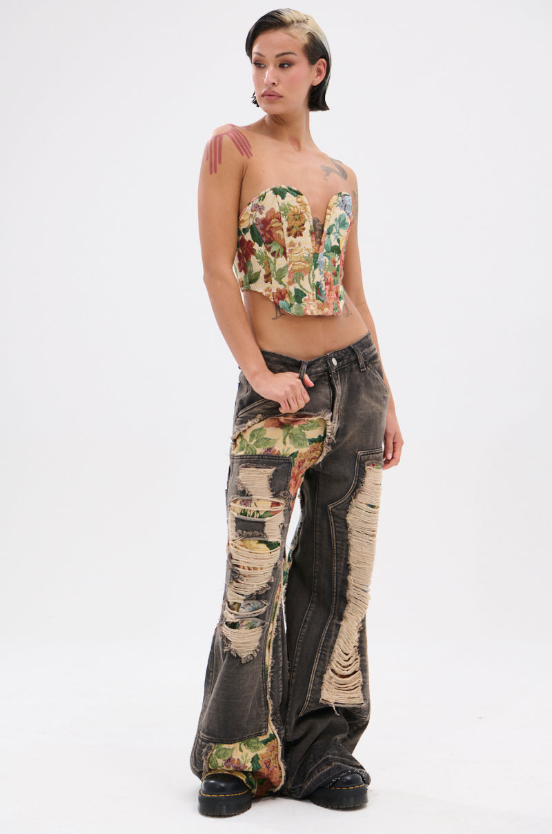 Confidently posed against a plain white background, a person flaunts high-waisted BRIGETTE DISTRESSED JEANS WITH JACQUARD DETAIL, featuring heavy distressing and floral fabric patches.