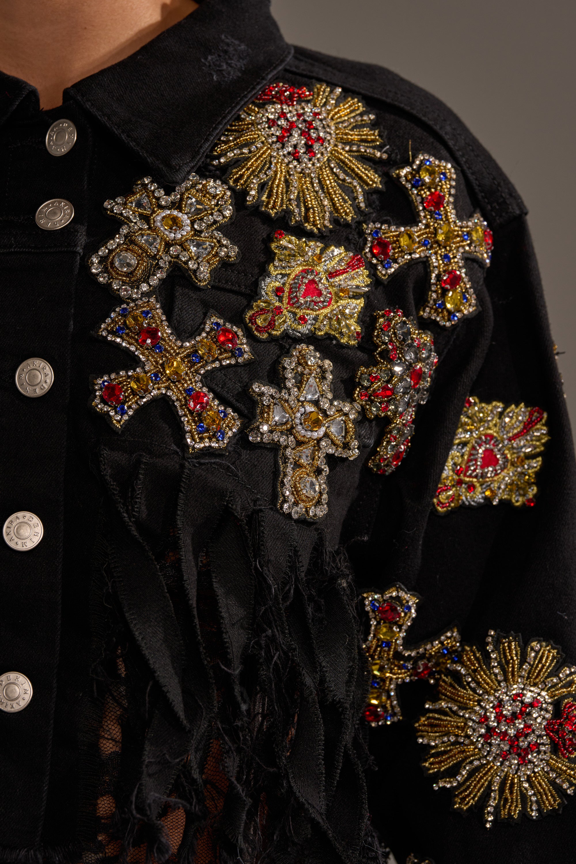 Close-up of the MAIN SQUEEZE CROPPED DENIM JACKET, detailed with silver buttons and ornate gold, red, and blue embroidered and beaded crosses, hearts, and starburst designs. 8