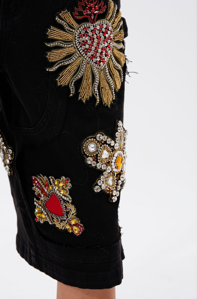 Close-up of the WILD AND FREE DENIM SHORTS in black, showcasing detailed embroidered and beaded patches with ornate heart and sun motifs in red, gold, and silver on a plain white background.