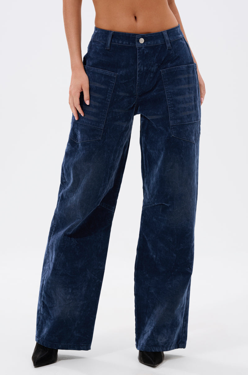A person wears the VALERIE VELVET EFFECT WIDE LEG PANT IN BLUE, featuring utility-style pockets and black heeled shoes, shown from waist to feet against a plain white background.