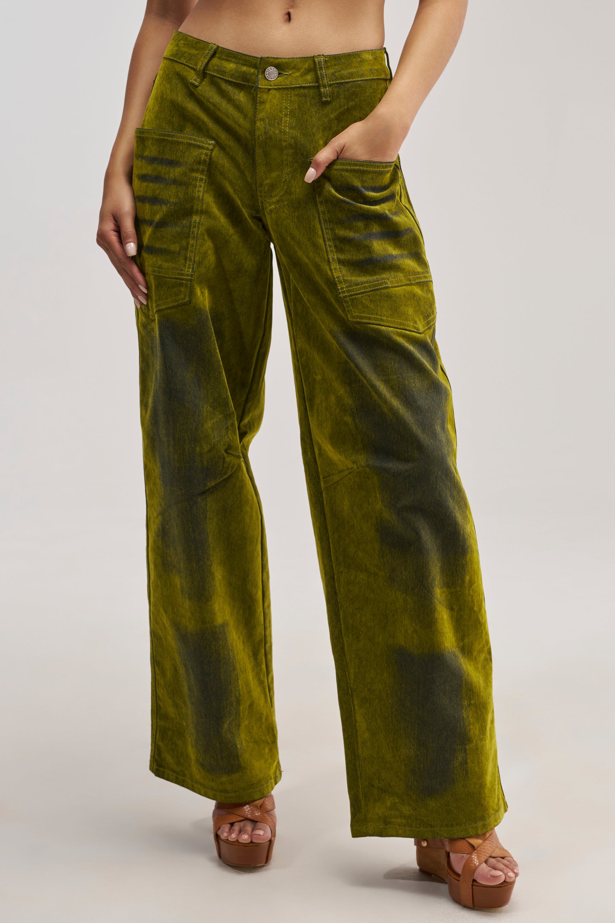 Wearing the VALERIE VELVET EFFECT PANT IN GREEN, which features a high-rise, wide-leg silhouette and large front pockets, a person stands against a neutral background in platform sandals.
