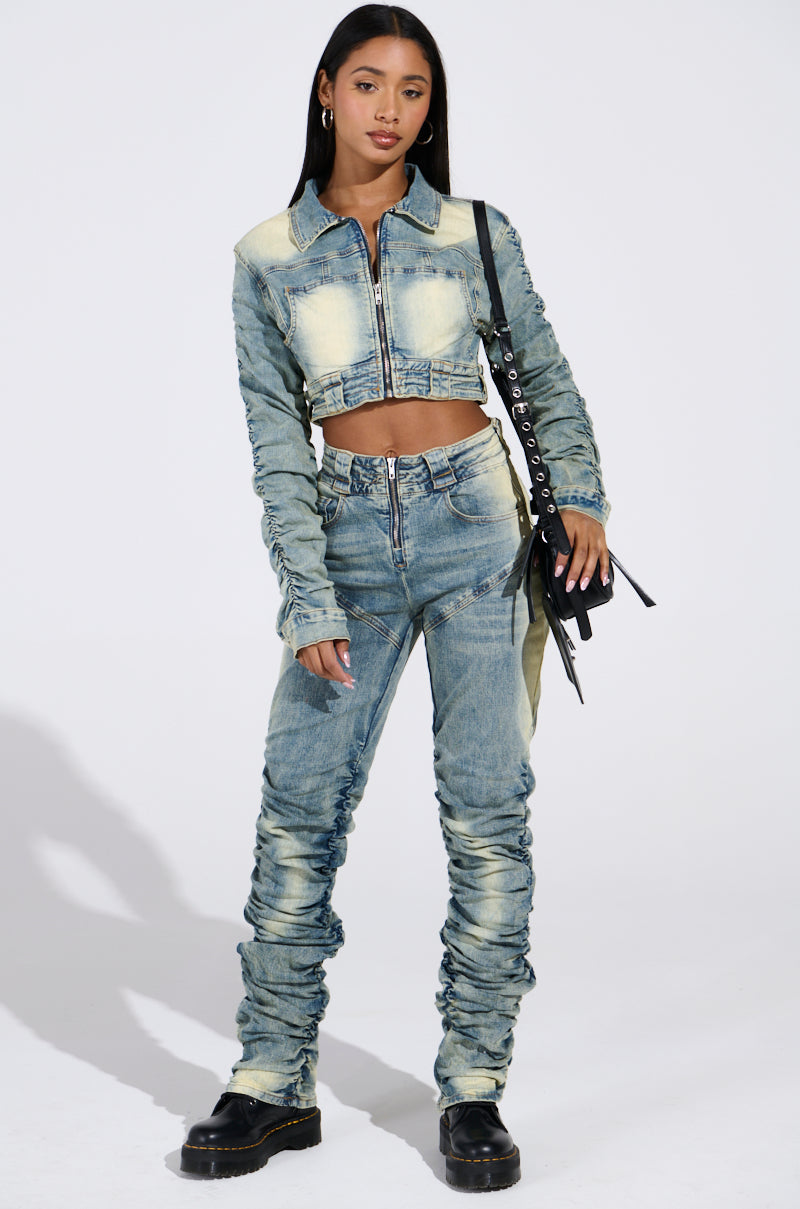 A woman confidently wears the UP ALL NIGHT DENIM PANT, paired with a cropped denim jacket. She holds a black and silver handbag while wearing black boots, set against a neutral background.