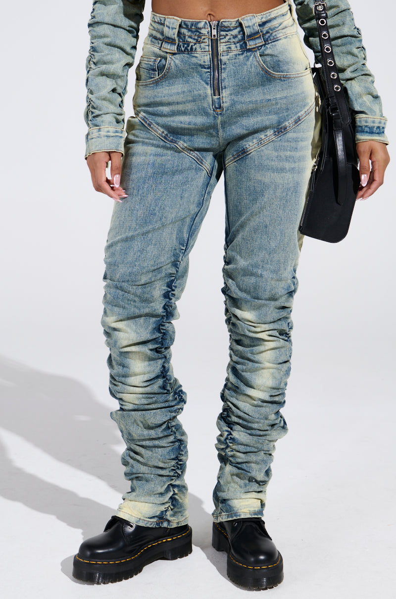The person sports UP ALL NIGHT DENIM PANT featuring high-waisted, stretchy fabric with zipper front and frayed detailing, paired with a matching denim jacket. They accessorize with a black bag and wear black chunky boots against a plain studio backdrop.