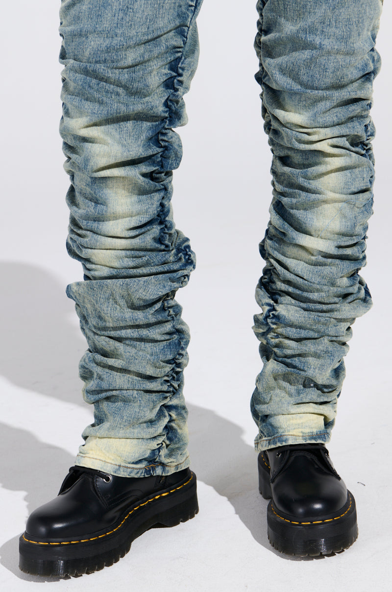 A person in Up All Night Denim Pants, ruched and faded blue, paired with black platform shoes with yellow stitching, stands on a pale surface.