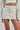 A person is wearing the STINGY WITH MY TIME MINI SKIRT, a casual, light grey drawstring mini skirt. It is paired with a matching long-sleeve top and a white crop top underneath. Made from a stretchy cotton blend, the high rise design highlights the lower part of the torso and upper legs.