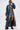 A model in the JULES DENIM TRENCH with ruched sleeves, denim shorts, black bra, futuristic sunglasses, knee-high black boots, and a small black handbag strikes a confident pose against a plain background.