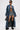 A person in oversized sunglasses, the JULES DENIM TRENCH with a longline silhouette, denim shorts, a black bikini top, tall black boots, and holding a small black handbag. Tattoos are visible on their torso and thigh.