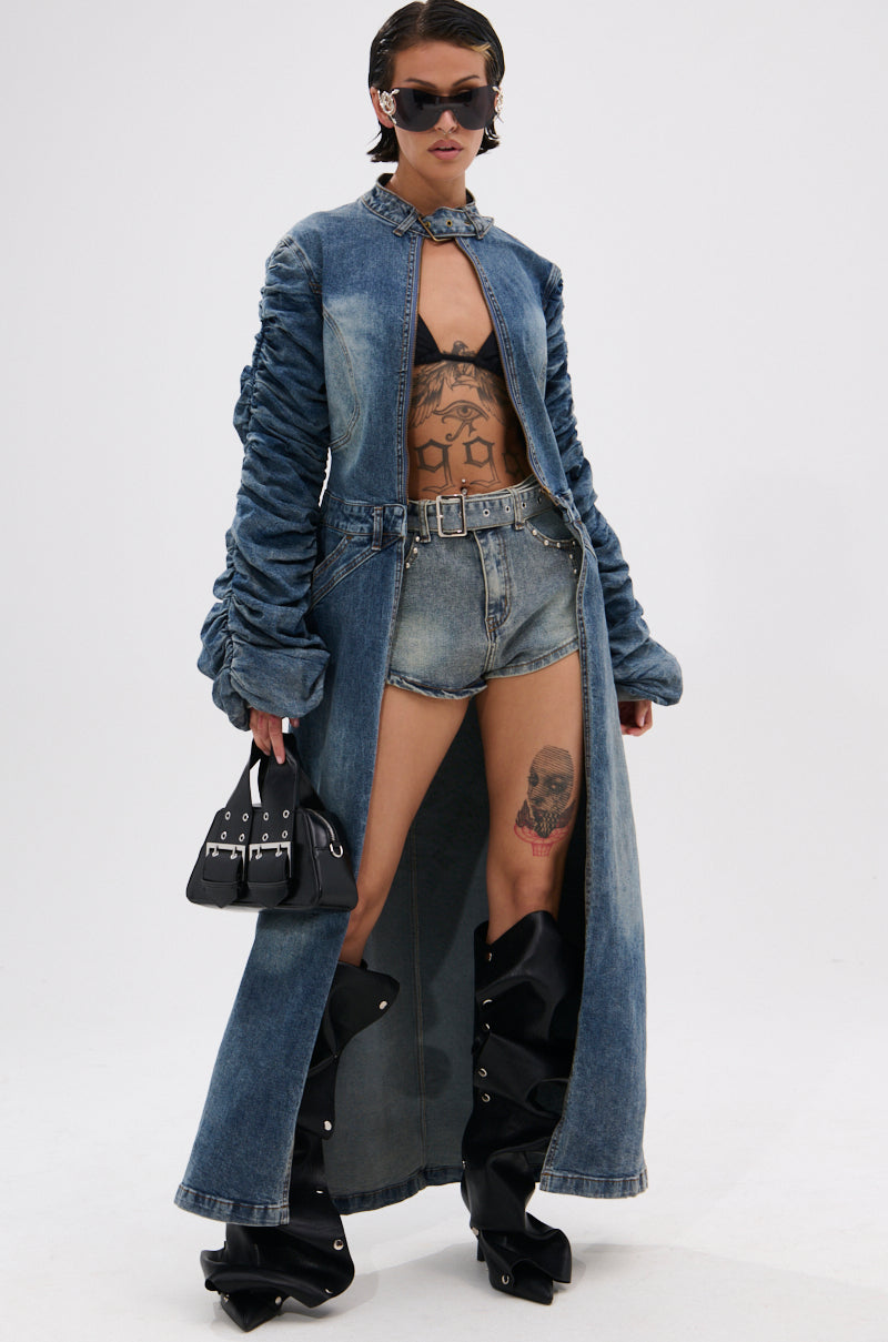 Wearing the JULES DENIM TRENCH in dark wash over a black bralette and denim shorts, paired with black platform boots, sunglasses, a choker necklace, and a small black handbag; tattoos accent legs and torso. 3
