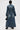 A person faces away wearing the JULES DENIM TRENCH, a dark-wash coat with ruched sleeves and a belted waist, styled with black heeled boots and a small black handbag against a plain white background.