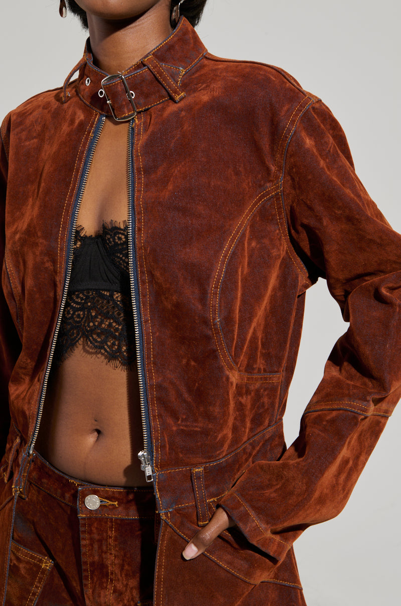 A person dressed in the VALERIE VELVET EFFECT TRENCH, partially open to reveal a chic black lace top. The trench's high-low silhouette enhances the coordinated pants, as they confidently place their hands on their hips, exuding style with assurance.