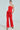 A person models a bold red strapless peplum top with BUSINESS CASUAL TROUSER IN RED, confidently standing with one hand in their pocket. Leopard print high heels complete the look against a neutral background, highlighting the outfit's striking elegance.