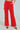 The woman showcases the Business Casual Trouser in Red, featuring high-waisted, wide-leg flair, front pleats, and a belt. Paired with leopard print heels for a chic professional look, she confidently rests one hand in her pocket.