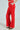A person models vibrant BUSINESS CASUAL TROUSER IN RED, complete with a matching belt and hands in pockets. Paired with pointed leopard print shoes, the look stands out against a plain light backdrop, emphasizing the chic and professional style.