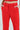 A person in BUSINESS CASUAL TROUSER IN RED stands with hands in pockets, showcasing flared pants with belt loops and a pleated front. A hint of a matching red shirt is visible against a plain white background.