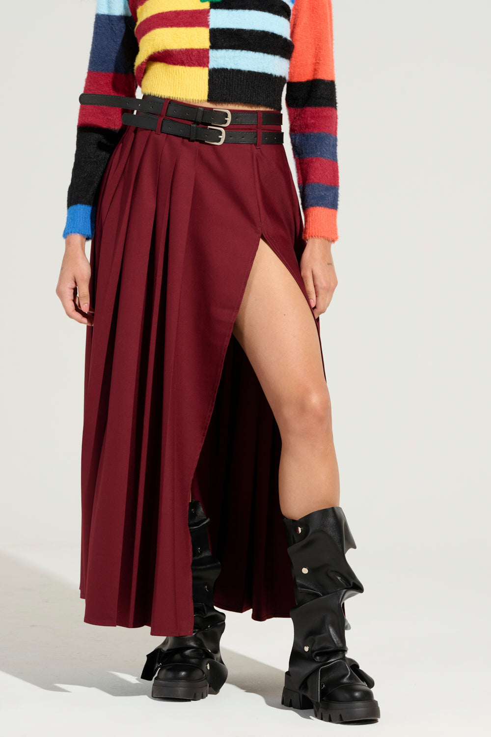 Someone is styled in a vibrant striped sweater paired with the FRENZIA MAXI SKIRT, featuring an ultra-high side slit. The look is finished with rugged black knee-high boots.