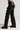 A person is modeling the SNAP OUT OF IT FAUX LEATHER PANT, featuring high rise fit and snap-button removable paneling that runs down the sides, creating a stylish ruffled effect. They are also wearing matching black boots adorned with metallic studs to complement the edgy look.