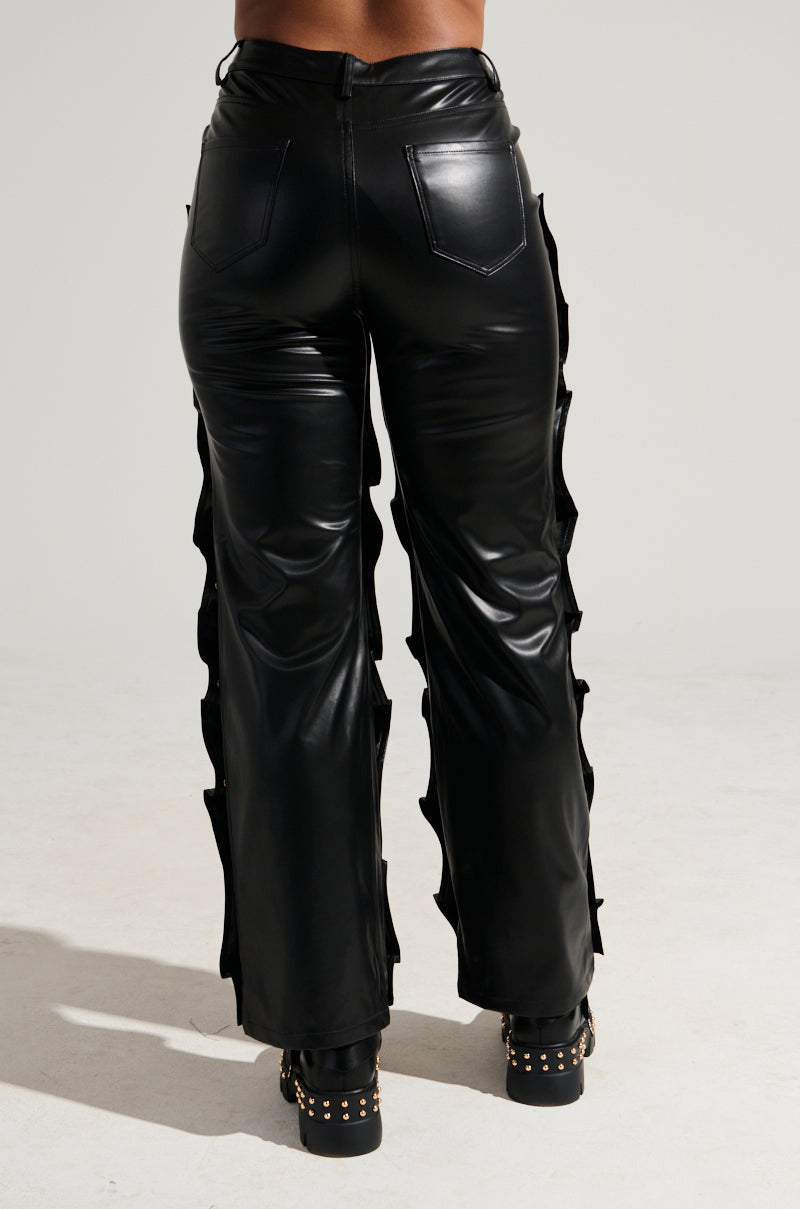 A person wearing the "SNAP OUT OF IT FAUX LEATHER PANT" with side cutouts and back pockets is standing facing away from the camera. The high-rise design adds a sleek touch to the shiny finish, paired perfectly with black platform shoes adorned with gold stud detailing. 4