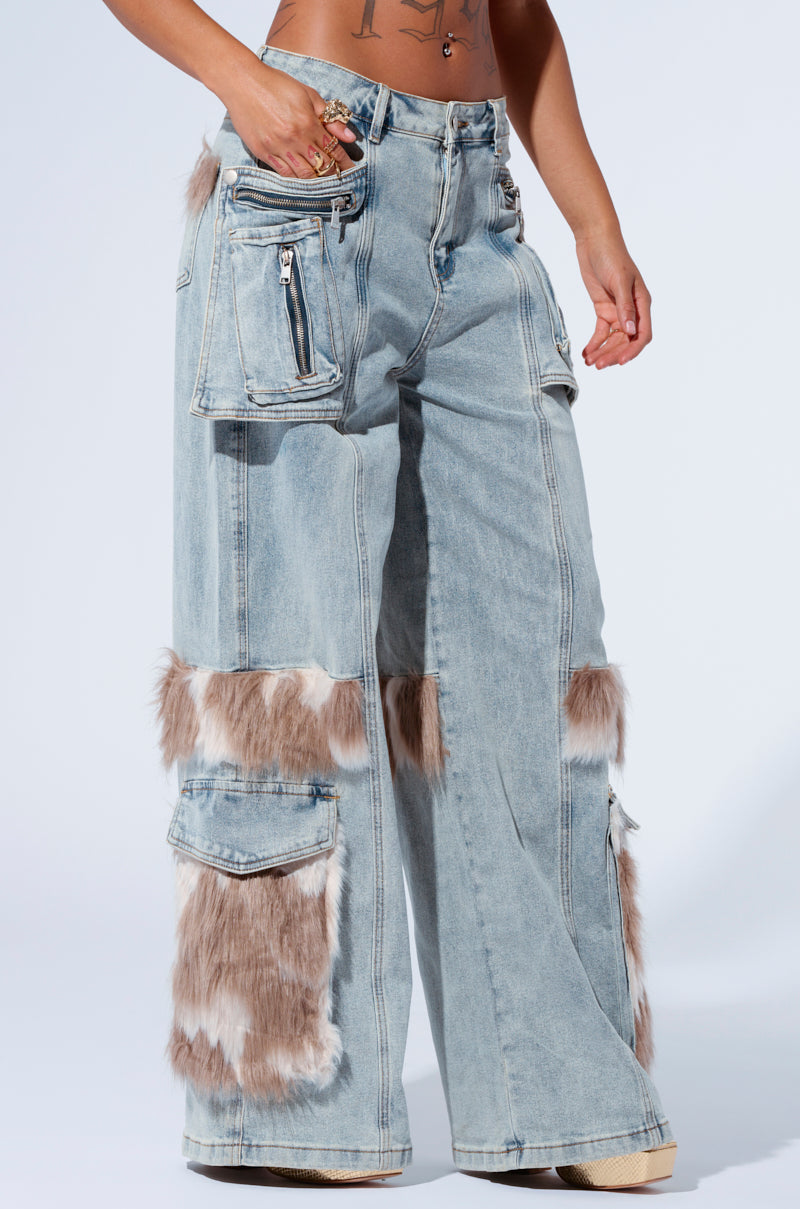 Person wearing FUR DENIM CARGO PANTS, featuring a light blue wide-leg design with a high rise. These unique jeans include faux fur trim patches and multiple pockets, such as zippered hip pockets and large flap thigh pockets. The denim is adorned with light brown and white fur accents on the knees and lower thighs.