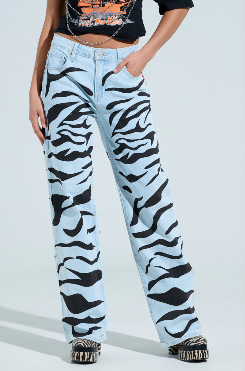 A person dressed in the SLEEPING WITH ROSES DENIM PANT featuring bold black zebra print, paired with a cropped black top and matching zebra-patterned shoes. The style is casual and trendy, set against a plain background.