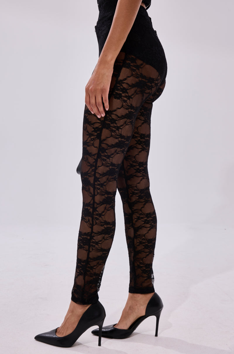 A person wears the FEEL FREE TO UNZIP ME LACE LEGGING, which features an intricate sheer floral pattern and a high-rise fit, paired with black heels. The lower half of the body is shown against a white background.