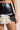 A person wearing the BACKIN IT UP MINI SKIRT WITH FUR, featuring a black faux leather design with a distinctive black and white fuzzy fur trim at the hemline. The image captures them from the waist to the upper thigh, focusing on the skirt's luxurious texture and fashionable style.