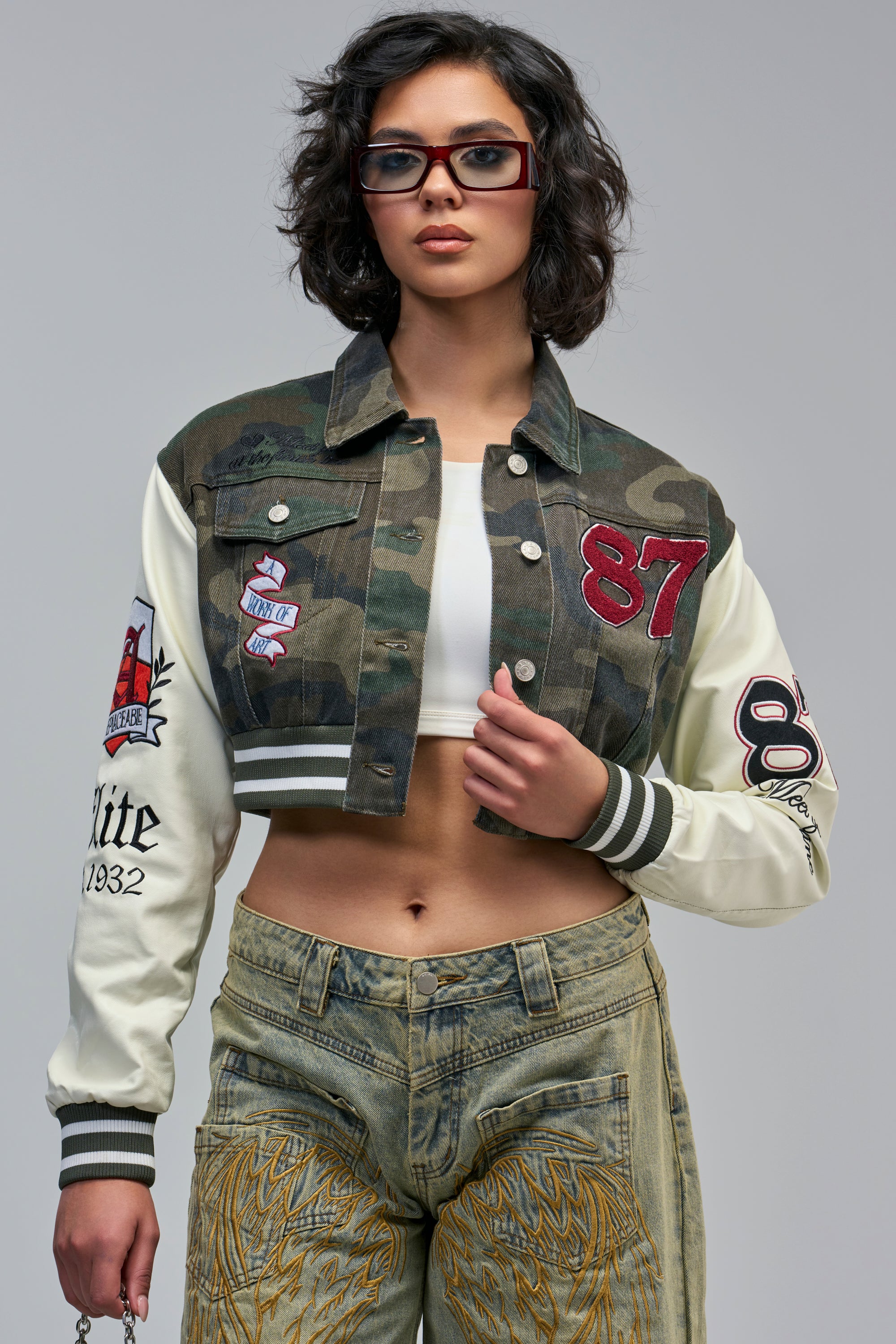 OFF CAMPUS CAMO DENIM VARSITY BOMBER, a cropped jacket with cream-colored sleeves and assorted embroidered patches.